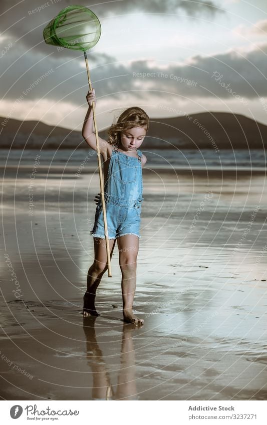 Curios kid with butterfly net walking barefoot on wet shore seaside cute childhood nature catch activity little natural coast beach vacation holiday resort sand