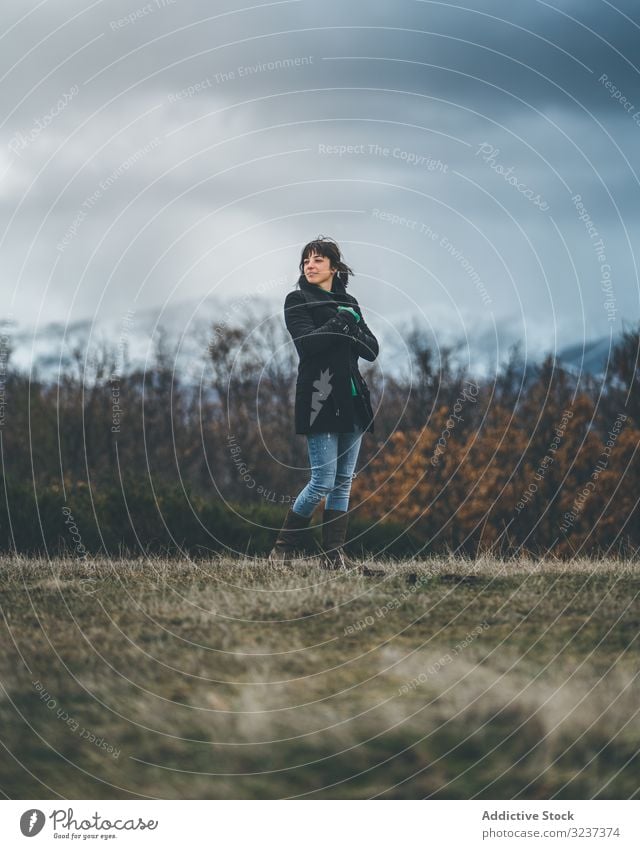 Young woman standing in autumn field country cloudy gloomy snow hill walk meadow forest female young alone frozen cold nature relaxation shivery journey