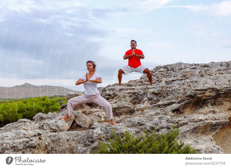 Couple meditating on rock couple meditation breath exercise tai chi clasped hands closed eyes nature sky cloudy training woman adult healthy fit yoga