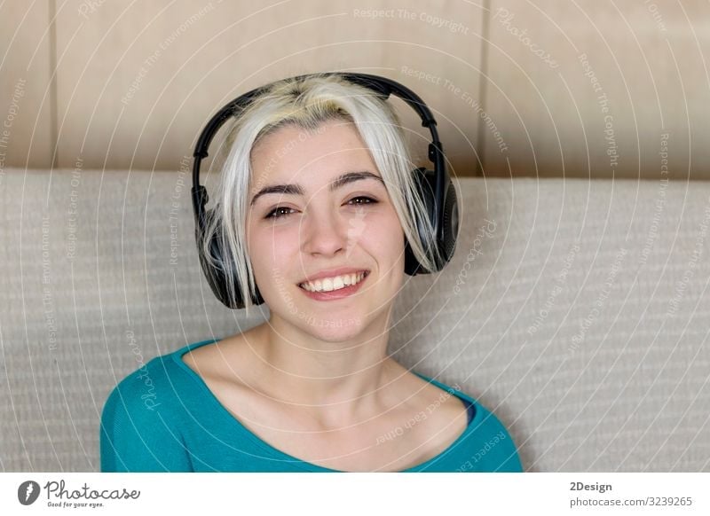 Close up of a smiling young woman with headphones while sitting on sofa and looking camera Lifestyle Happy Beautiful Face Relaxation Leisure and hobbies