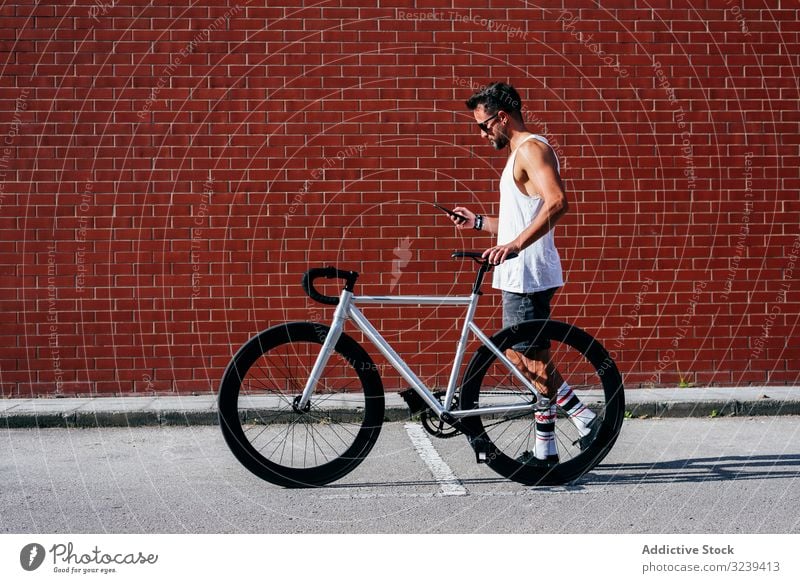 Sportive man with bicycle using phone bike stand mobile phone modern sportive active summer male sunglasses cyclist smartphone message texting checking reading