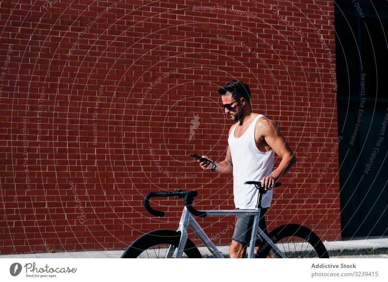 Sportive man with bicycle using phone bike stand mobile phone modern sportive active summer male sunglasses cyclist smartphone message texting checking reading