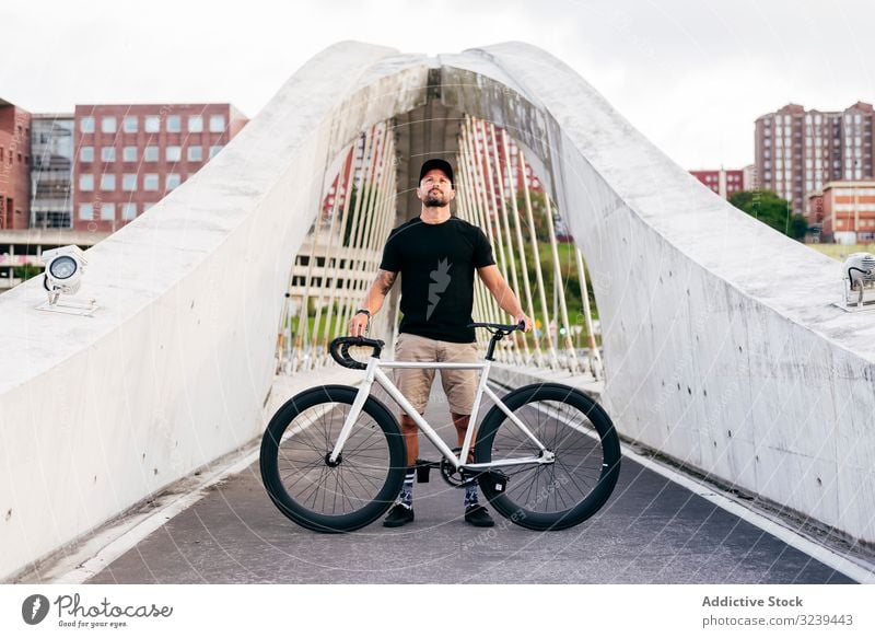 Cheerful man with bicycle standing on footbridge bike city ride modern active sportive summer male adult happy cheerful smile beard cap cyclist recreation