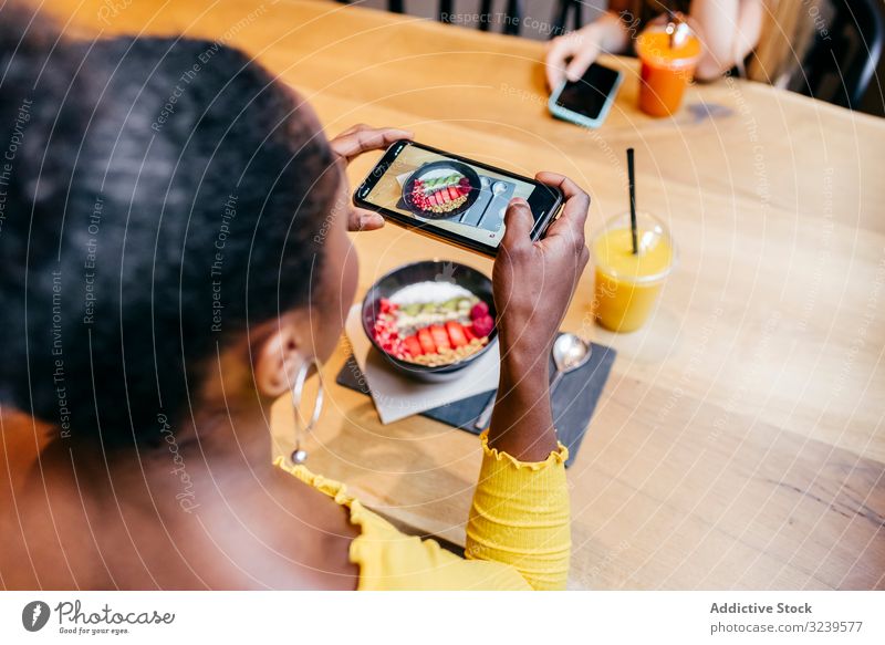 Woman taking picture of food with smartphone woman taking photo smoothie table bowl juice healthy food photography female african american black mobile