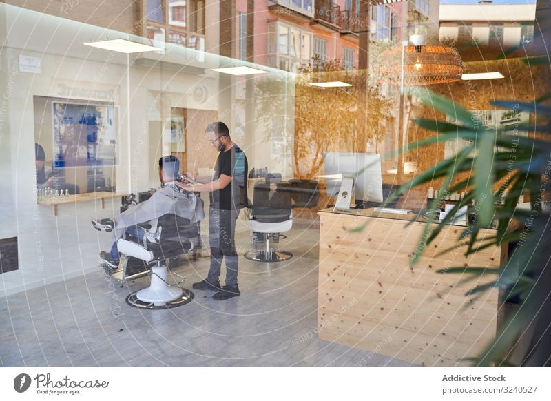 View of a barber shop from outside the enclosure with a barber inside cutting a client's hair design reflexion window storefront street decoration outdoors