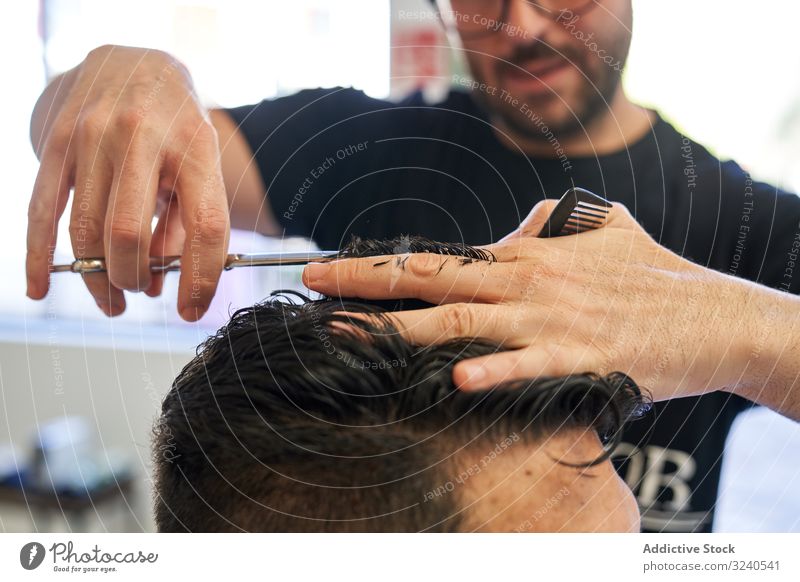 Detail of a hand from a barber cutting hair with scissors and a comb to a customer with the blur in the background haircut salon client hairdressing human