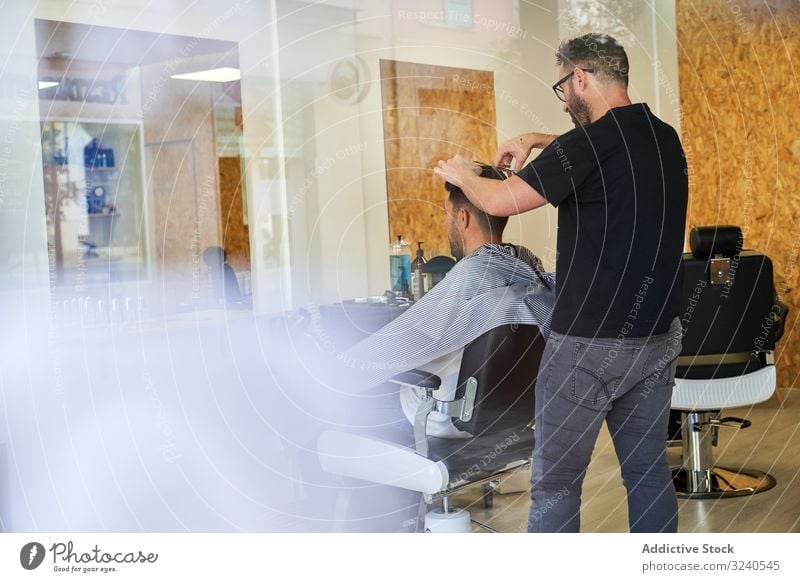 View of a barber shop from outside through fogged glass with a barber inside cutting a client's hair vertical reflexion window storefront street outdoors shaver