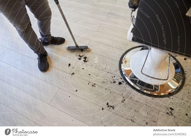 Barber sweeping with the broom the hairs of a customer that are on the wooden floor clipping salon barber barbershop business hairdresser beauty nobody