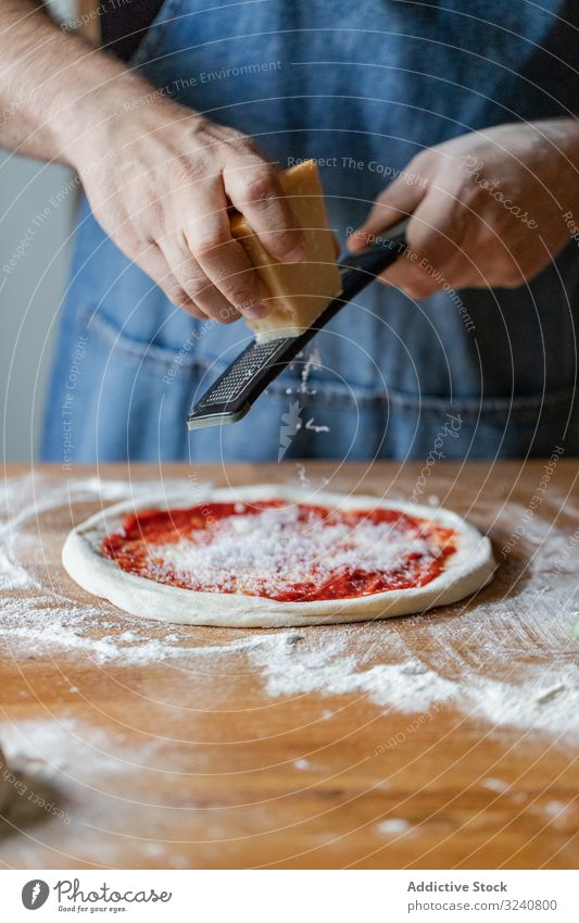 Crop cook grinding cheese on pizza man dough sauce flour soft fresh cuisine kitchen preparation food chef italian male apron raw uncooked pizzeria cafe