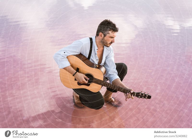 Musician with guitar on pink sandy water musician rest sit sky cloud dreamy wistful serious man reflection acoustic beach sea cloudscape majestic breathtaking