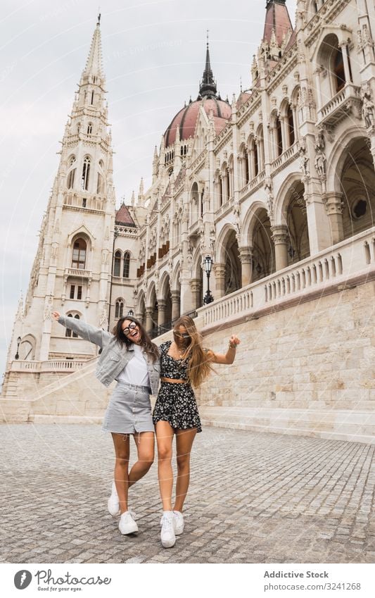 Funny girl friends on old square with dome buildings women stroll tourist architecture embrace travel tower fun trendy happy style laugh budapest hungary shape