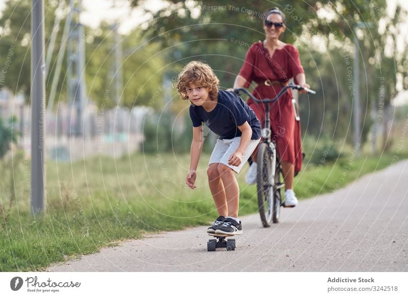 Mother and son riding along park path mother ride skateboard bicycle together fun family happy boy woman child kid summer joy glad pleasure smile cheerful