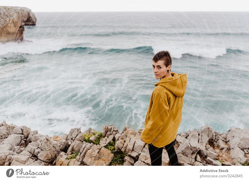 Person in yellow hoodie on stony shore solitude travel wave stone watching dream harmony standing contemplation lonely thoughtful sea ocean horizon freedom