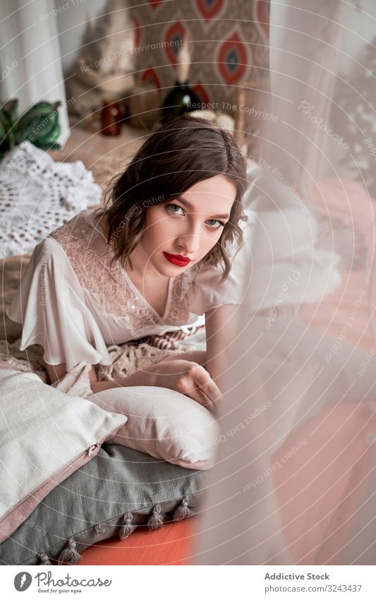 Gorgeous woman with red lips in white dress looking at camera while sitting on floor beside sofa wedding dress vintage chic elegant bride beauty trendy makeup