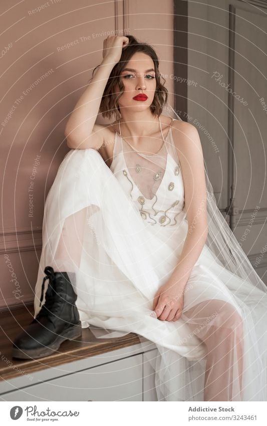 Attractive adult confident lady in white dress and military black shoes looking at camera woman wedding dress red lips provocative elegant cool rude beauty