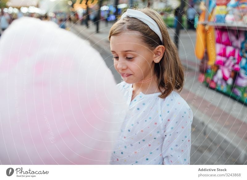 Cheerful girl eating cotton candy on street candyfloss stall smile city fair joy kid happy child urban town sweet fun vendor buy sell sidewalk pavement casual