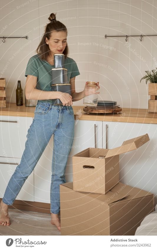 Careful woman holding containers with hand and taking cans out of box apartment unpack kitchen moving female cardboard carton home delivery receive opening