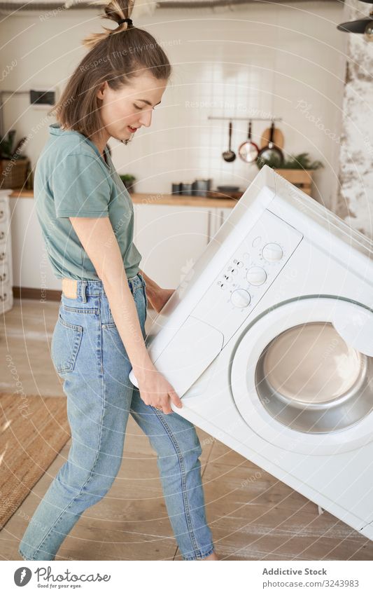 Joyful strong woman carrying washing machine in kitchen moving fun appliance new home delivery activity happy property heavy cleaner helping house beginning