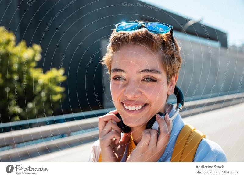 Playful trendy woman on street in sunshine covering camera with hands bright smile playful sunglasses millennial headphones happy charm human face vivid