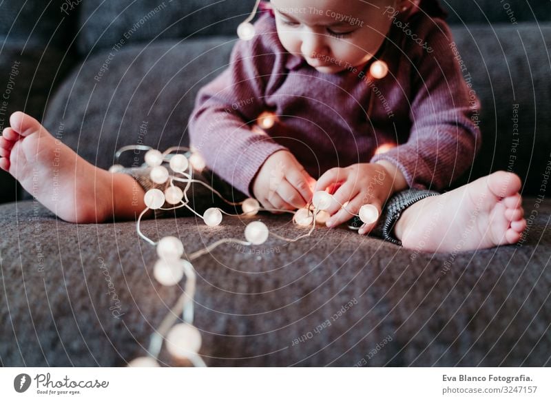 portrait of beautiful baby girl at home sitting on the sofa playing with a garland of lights Lifestyle Joy Happy Leisure and hobbies Playing Flat (apartment)