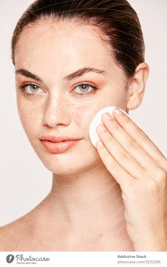 Peaceful female applying toner on radiant face with sponge - a