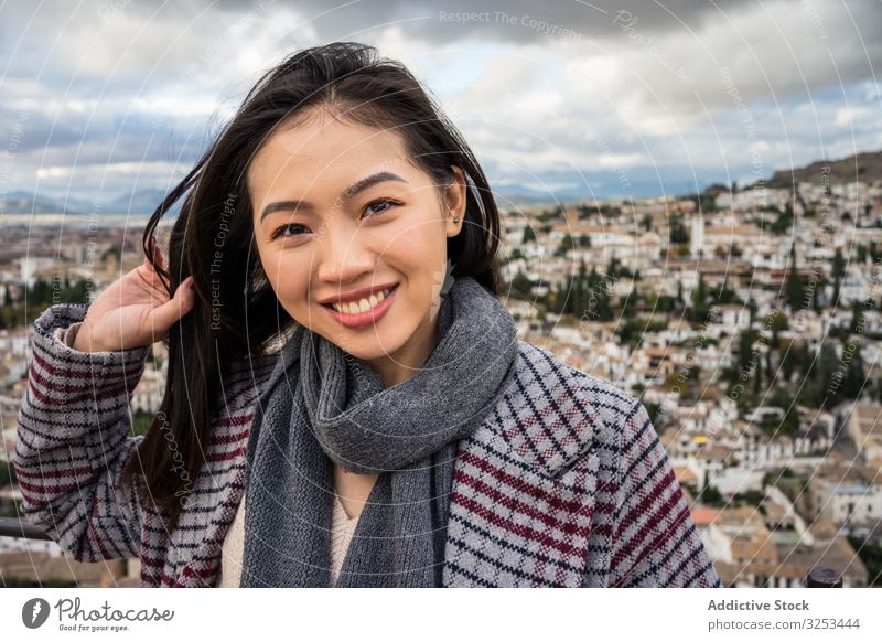 Cheerful ethnic woman visiting ancient city tourism cloudy sky smile female stylish trendy architecture asian travel trip happy cheerful overcast delighted