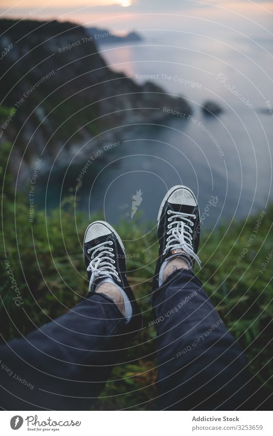 Person legs on seascape background during sunset person man feet edge nature landscape scenic picturesque water bay rock hill idyllic sneakers enjoy serene rest