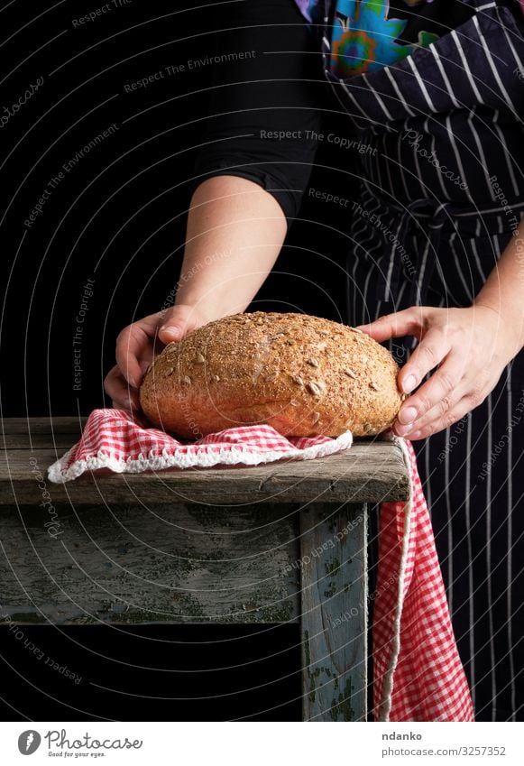 woman holds in her hands baked round rye bread Dough Baked goods Bread Table Kitchen Human being Woman Adults Hand Wood Make Dark Fresh Brown Red Black White