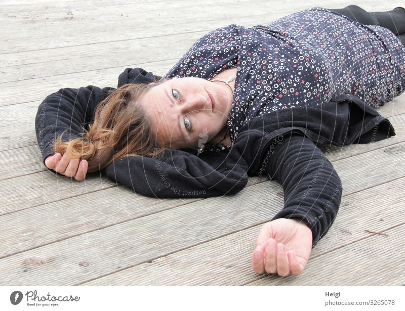 Woman with long brunette hair and dark and patterned clothes lying on a wooden floor Human being Feminine Adults 1 45 - 60 years Clothing Dress Jacket Brunette