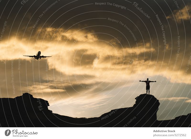 Human silhouette on hill delighting in view of aircraft in sky airplane standing mountain enjoy freedom raised hands clouds sunset nature beautiful carefree