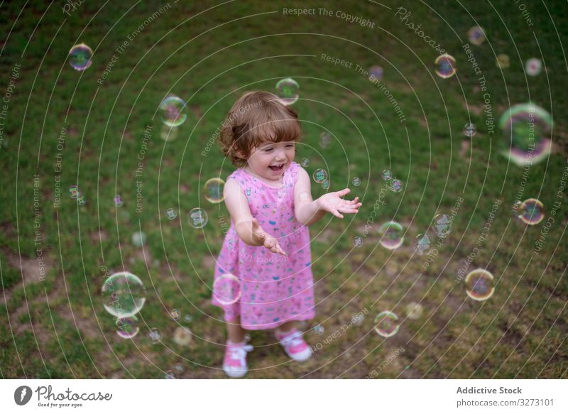 Joyful girl playing with colorful bubbles in grass soap childhood joyful fun adorable cheerful park playful enjoyment action wet little motion recreational blow