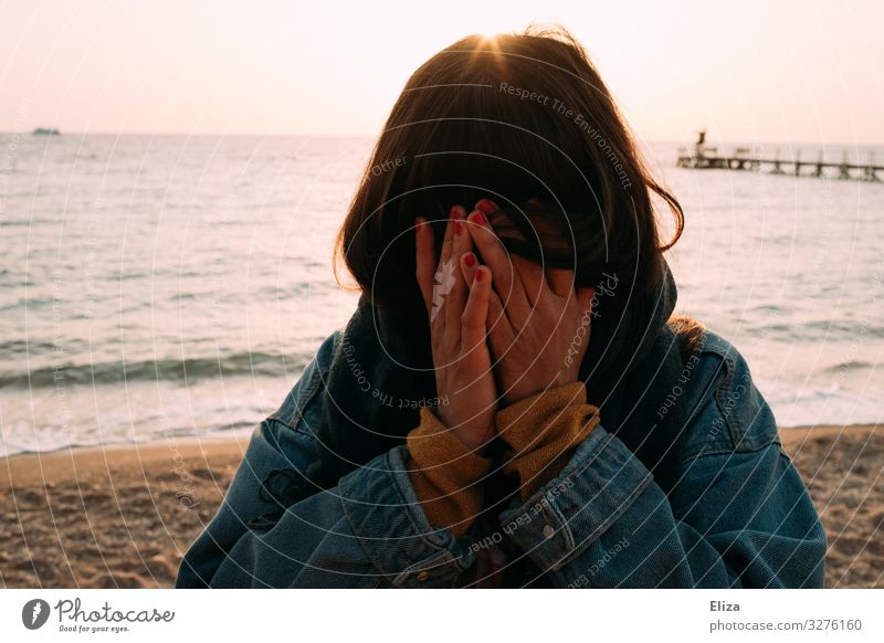 A young woman stands on the beach and hides her face in her hands. Pain, grief, anonymous. Feminine Young woman Youth (Young adults) Woman Adults 13 - 18 years