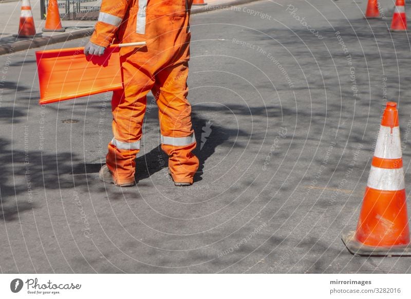 orange suited man directing traffic with orange flag on a blacktop road Work and employment Profession Construction site Industry Tool Human being Man Adults