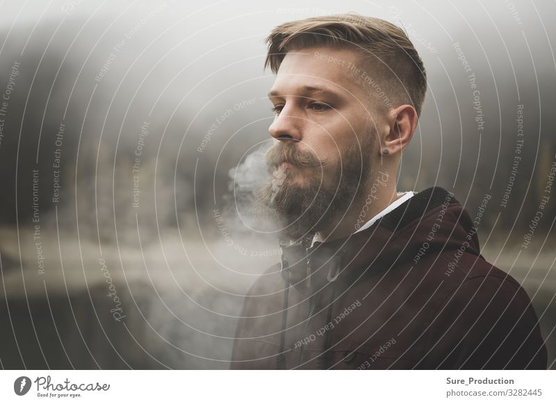 Pretty bearded man smokes cigarette Blows out steam through nostrils Smoke Man more adult Earnest Beard youthful Caucasian Style stylish background Cigarette