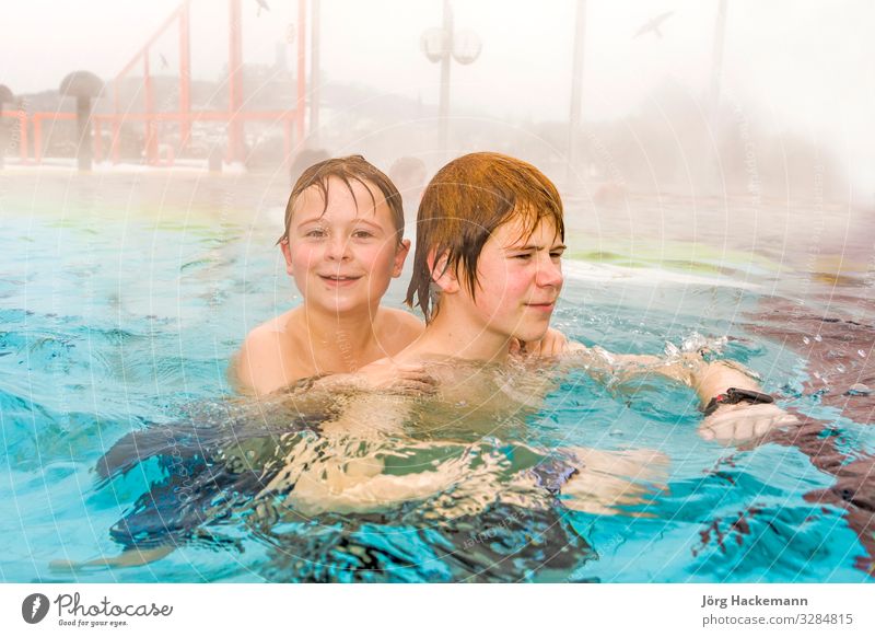 Young brothers are swimming in the outside area of a thermic pool in Wintertime in warm water, it is foggy Joy Happy Spa Swimming pool Leisure and hobbies