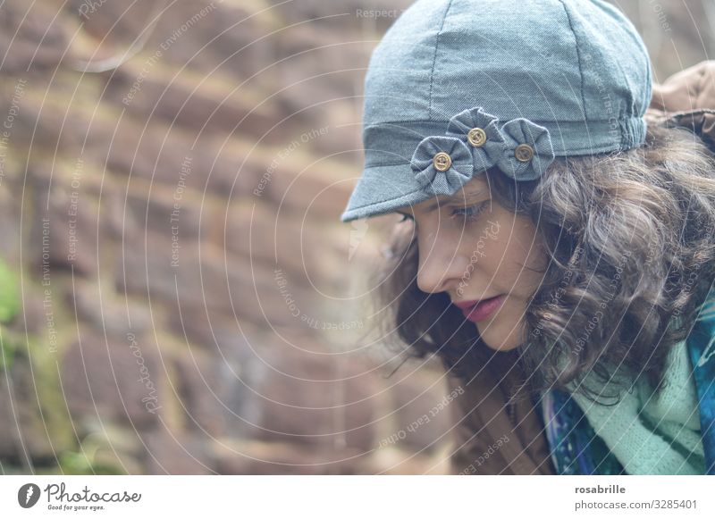 young, pretty, curly, brunette woman with hat, jacket and scarf in profile looks down thoughtfully Woman Brunette youthful Curl Curly Meditative Think brood