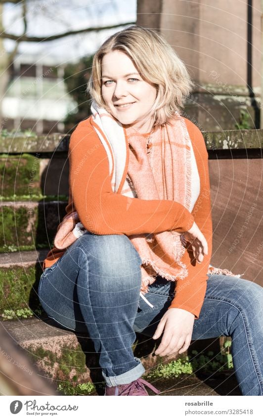 Portrait of young pretty blonde woman in jeans with orange sweater and scarf on stairs in full sunlight Woman Blonde youthful Bob hairstyle Scarf Autumn Day