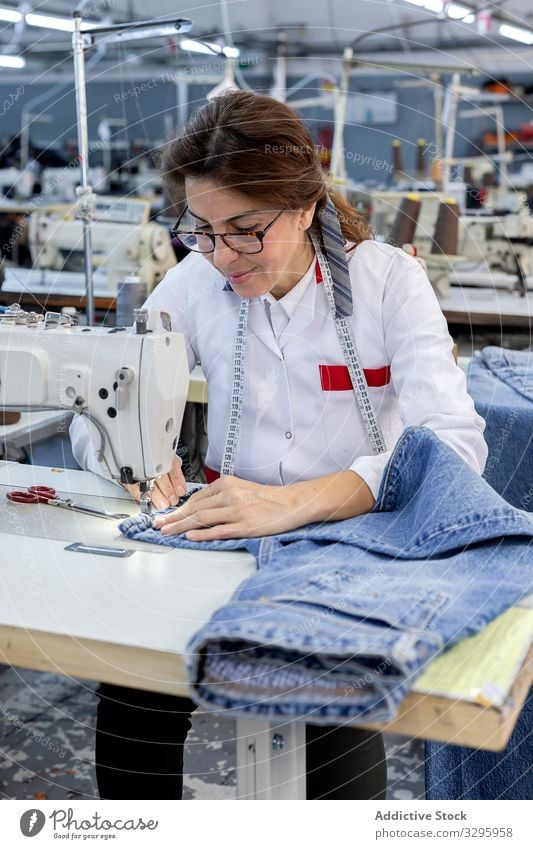 Woman's hands in textile factory sewing on industrial sewing machine. industry clothing manufacturing worker woman fabric pants blue jeans occupation production