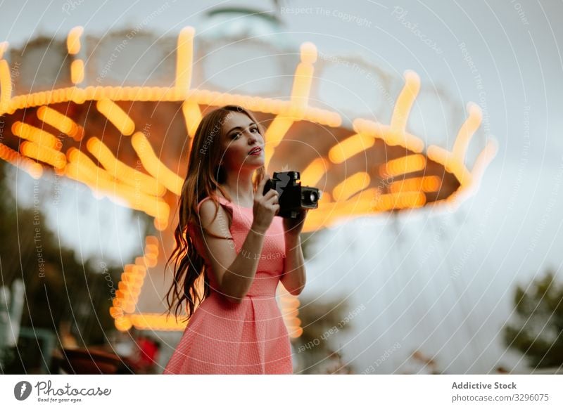 Millennial woman taking picture with camera in amusement park taking photo funfair trendy romantic dress pink teenager carousel millennial fashion style female