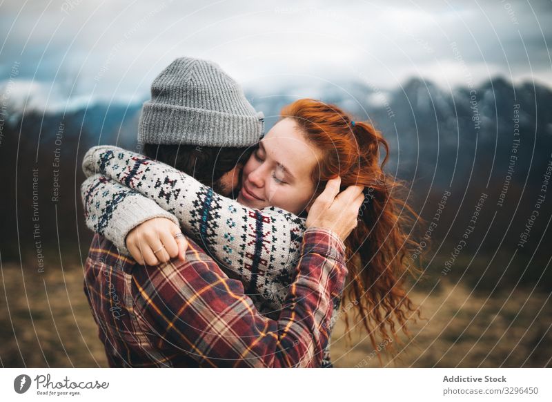 Charming red haired woman embracing man in mountains with closed eyes couple hugging bonding amorous romantic relationship lawn travel adventure tender