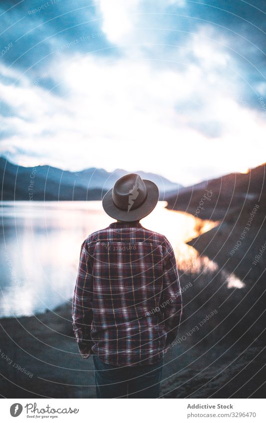 Man looking at lake reflecting clouds traveler mountain hat nature adventure tourist vacation landscape freedom wanderlust crystal extreme breathtaking holiday