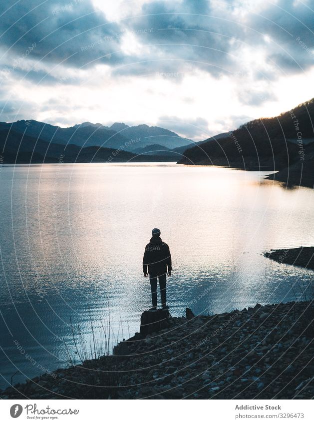 Man looking at lake reflecting clouds traveler mountain hat nature adventure tourist vacation landscape freedom wanderlust crystal extreme breathtaking holiday