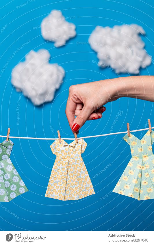 Crop woman attaching origami dresses to rope concept hang clean laundry sky cloud female bright vivid vibrant paper mockup creative art craft lady apparel