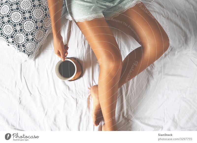 Young woman enjoying her coffee while sitting in bed. Coffee Lifestyle Joy Beautiful Relaxation Leisure and hobbies Bedroom Woman Adults Body Hand Legs 1