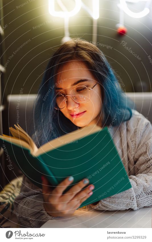 Young adult mixed asian female with blue hair holding a book in a cafe with neon lights, selective focus Beauty Photography Book Café colorful hair Face Woman
