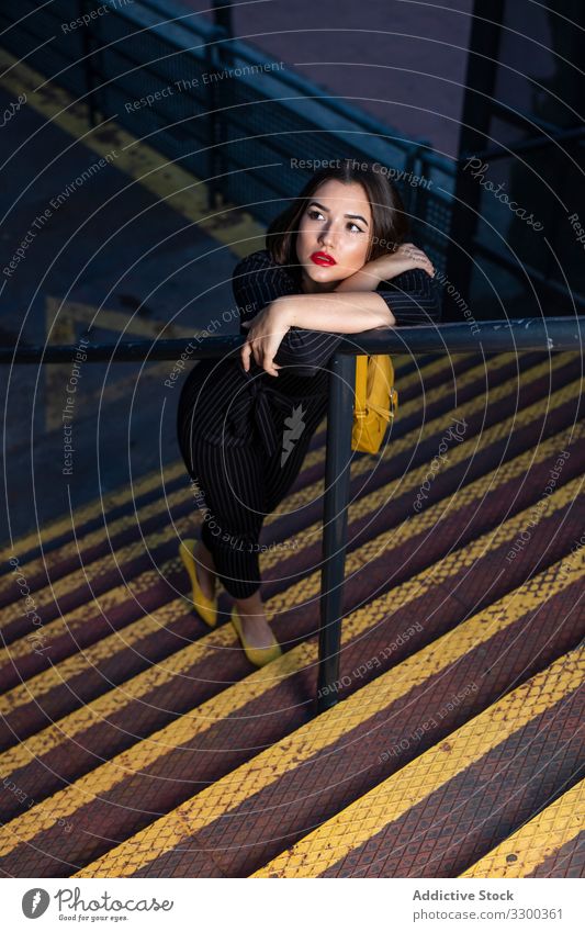 Woman in stylish outfit leaning on handrail at staircase woman fashionable trendy dusk shadow clothing city street standing young cap lady brunette accessory