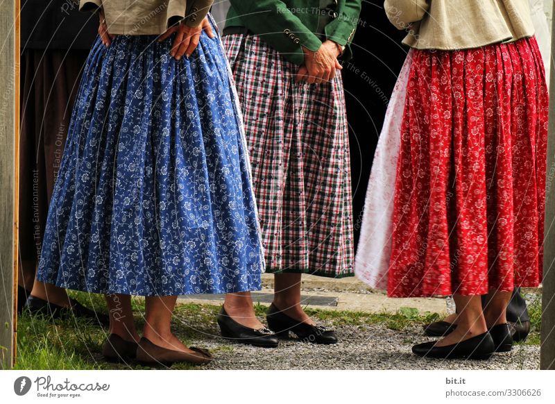Three women in dirndls with skirts, aprons, patterns, checks and flowers stand together in Bavaria for a round of talks. A group of ladies in traditional costume stand together for village gossip, conversation, ratcheting, exchange, morning pint gathered in a circle.