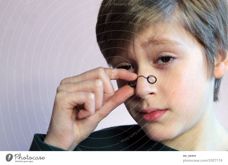 Boy looks through small glasses with sceptical eyes Looking monocle Eyeglasses Looking into the camera Portrait photograph Human being Masculine Face