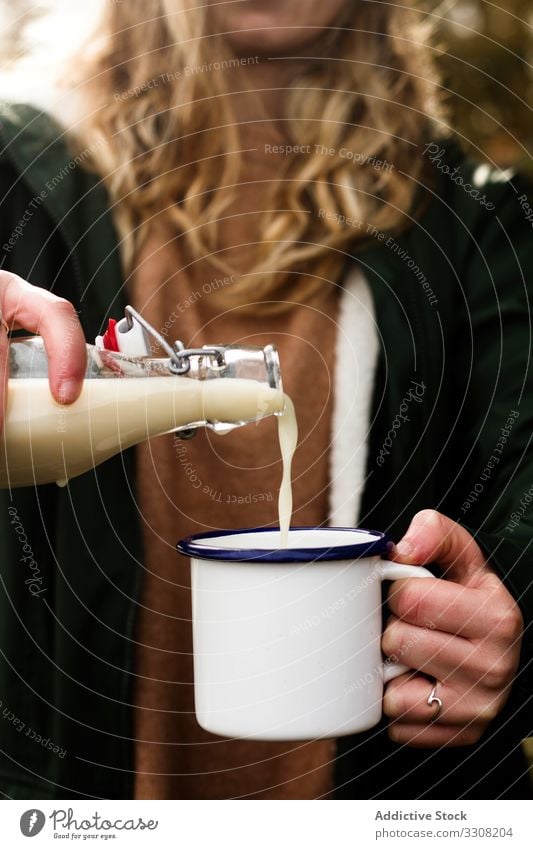 Anonymous woman filling mug of milk during picnic pour dairy bottle casual female rural countryside autumn drink cup beverage prepare tasty ingredient cream