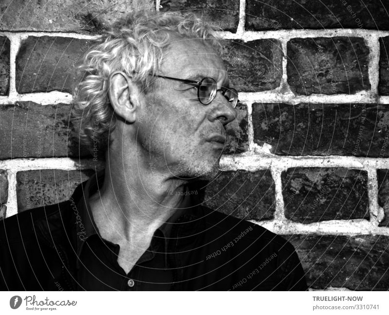 Not lifted | Known Photocase icon, senior user, man with glasses visiting Potsdam in front of a brick wall in black and white profile with silver curls, black polo shirt, looking strictly to the right